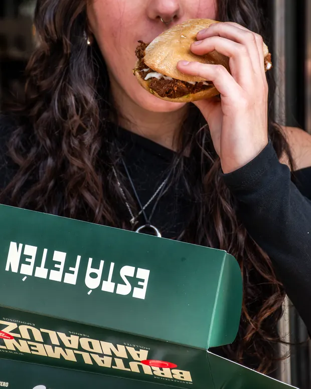 Clienta comiendo un mollete junto a la caja verde de Estafetén